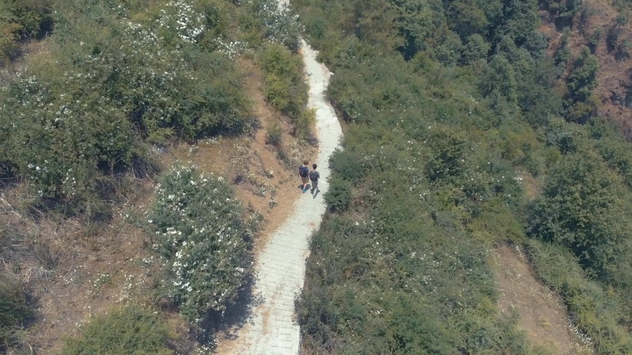 Two boys walk a concrete path on the side of a mountain.