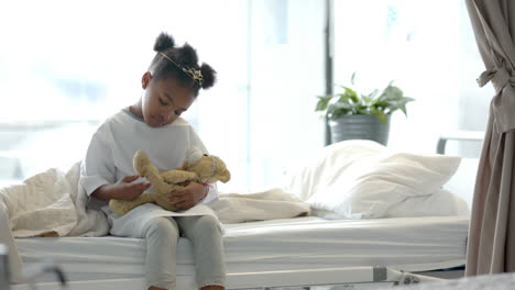 african american girl holding mascot in hospital bed, slow motion