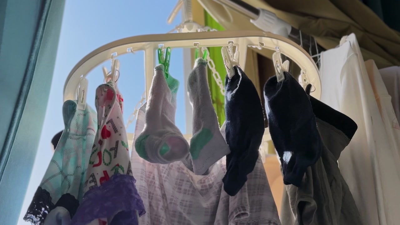 Close-up of socks and garments hanging on a circular drying rack near a window indoors, lit by natural daylight, showing everyday household laundry care in a home setting.