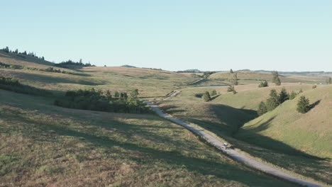 truck drives on dirt road through scenic grassland and hills, aerial orbit