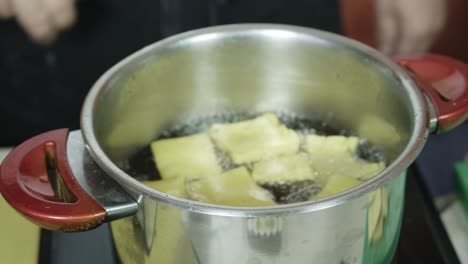 el chef toca el filtro de malla de alambre en el lado de la olla con panela de fritura de aceite hirviendo