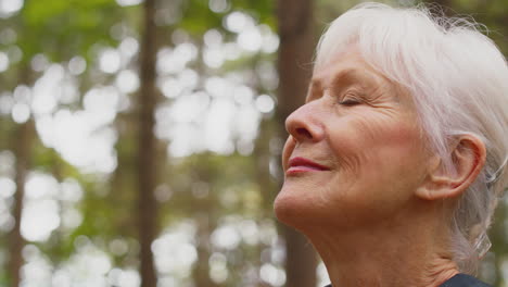 active retired senior woman walking in woodland countryside wearing backpack