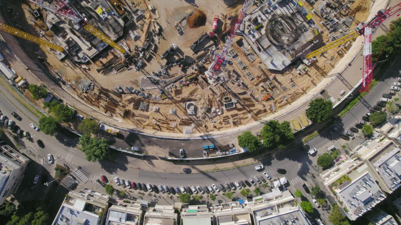 una vista aérea de una grúa torre en un sitio de construcción en una gran plaza de la ciudad mientras gira a su alrededor - toma de arriba hacia abajo