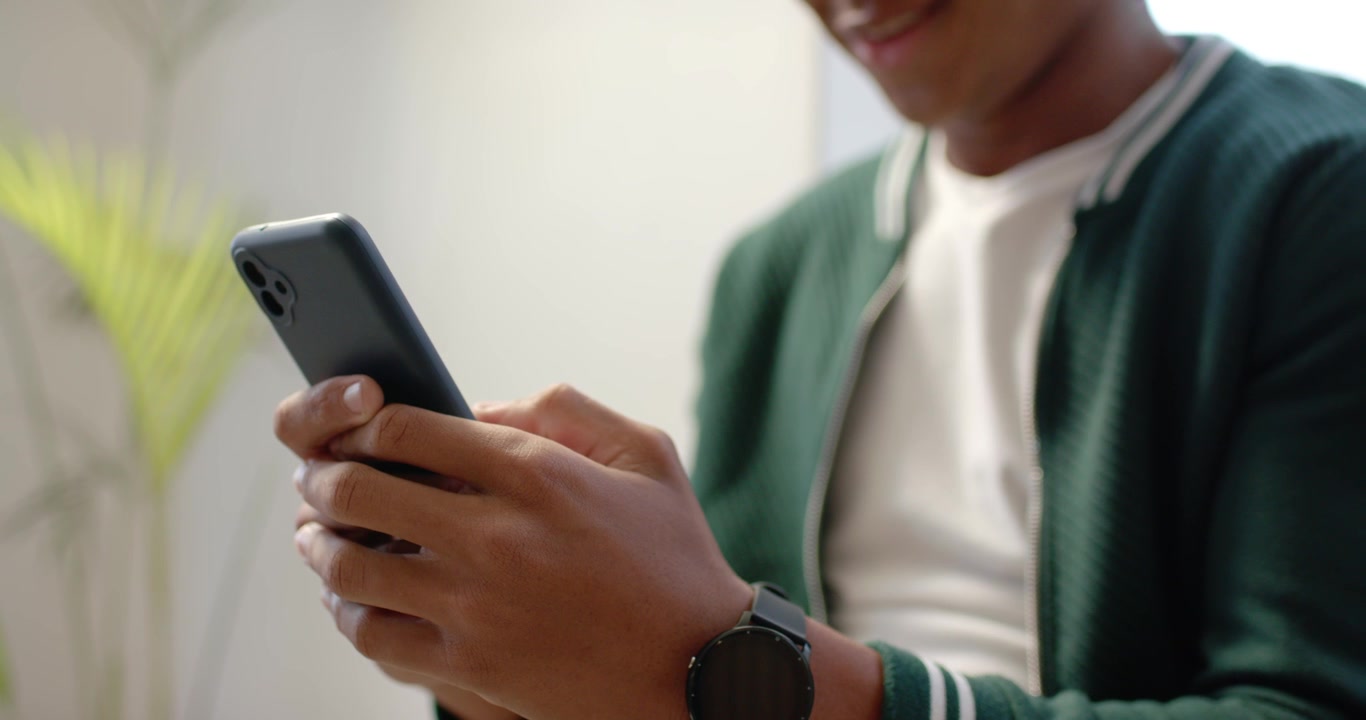Man is holding phone thumbs poised then tapping and scrolling in living area while reading text