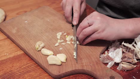 woman's hands with a knife chops two cloves of garlic on a chopping board