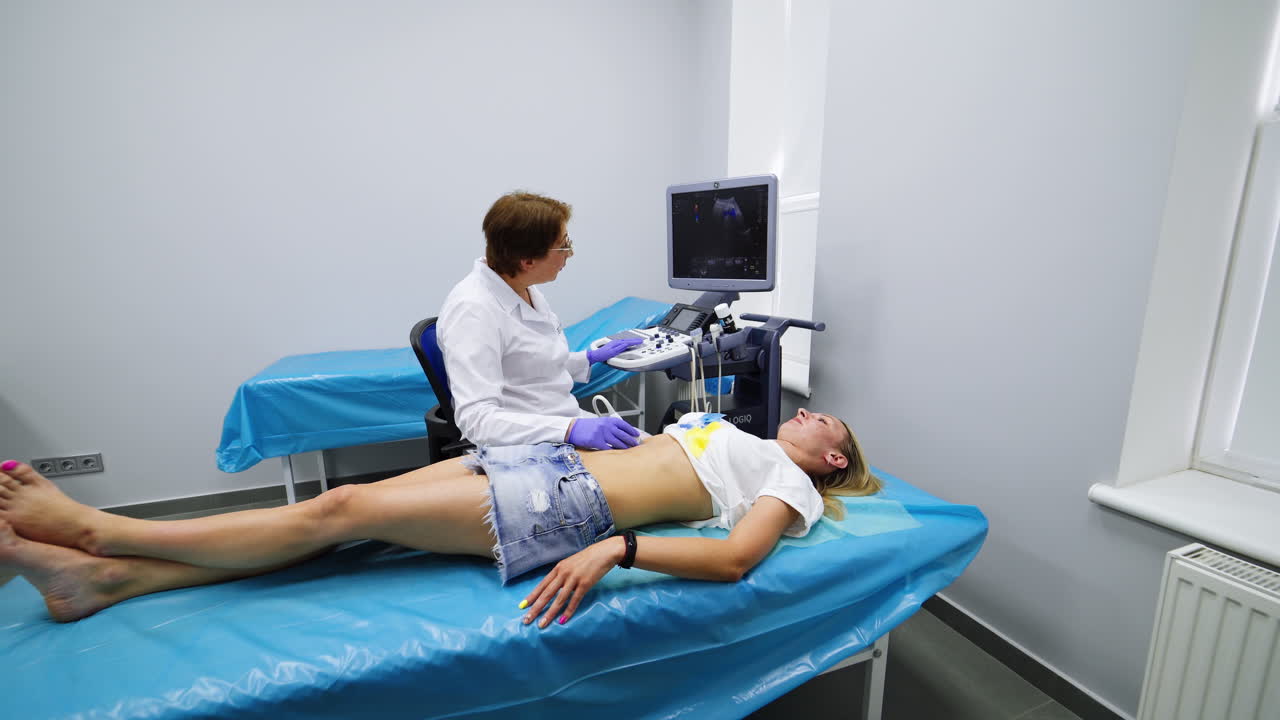 Female doctor in glasses performs check up for a female patient. Ultrasonic diagnostics for inner organs.