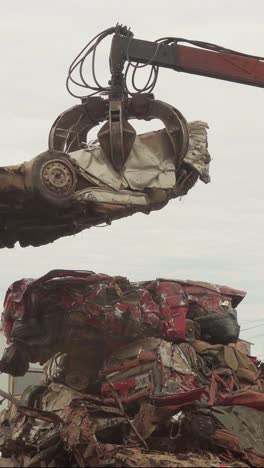 vertical view of a hydraulic claw placing a crushed car on a pile in a junkyard