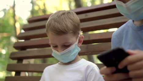 teenagers in medical masks play with smartphones in the park 02