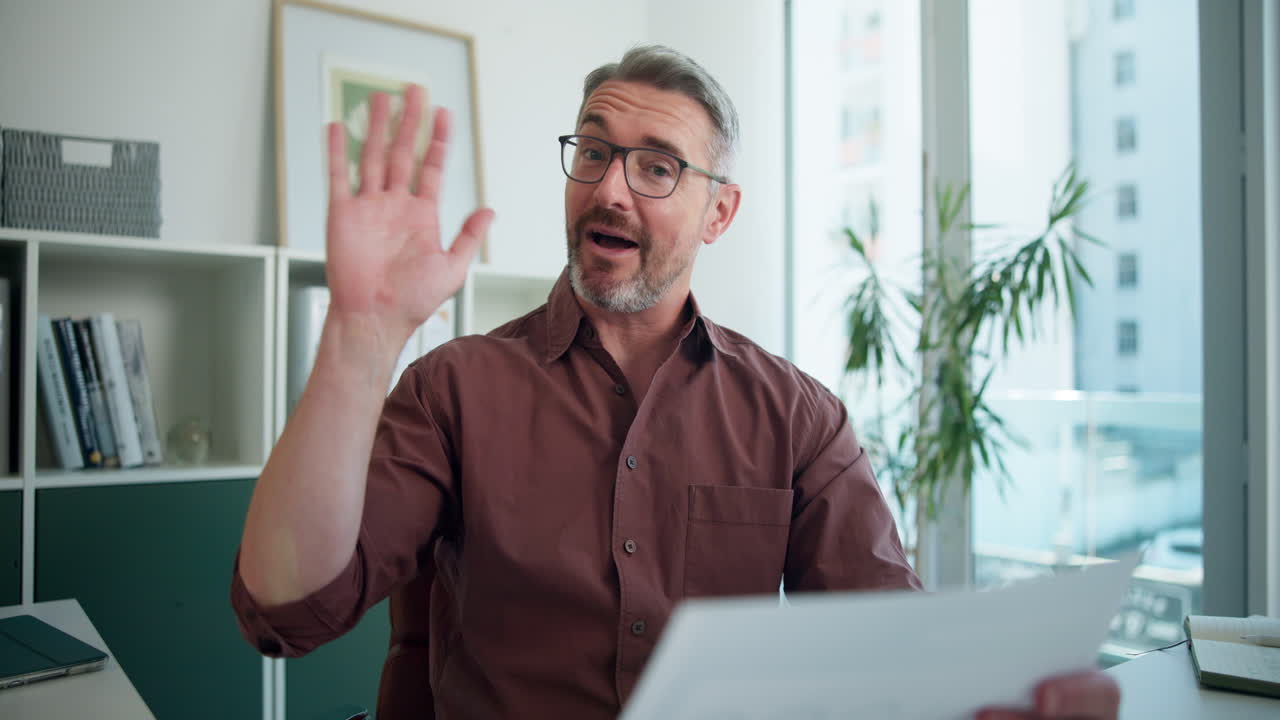 Homme d'affaires mûr parlant et faisant signe lors d'un appel vidéo au bureau