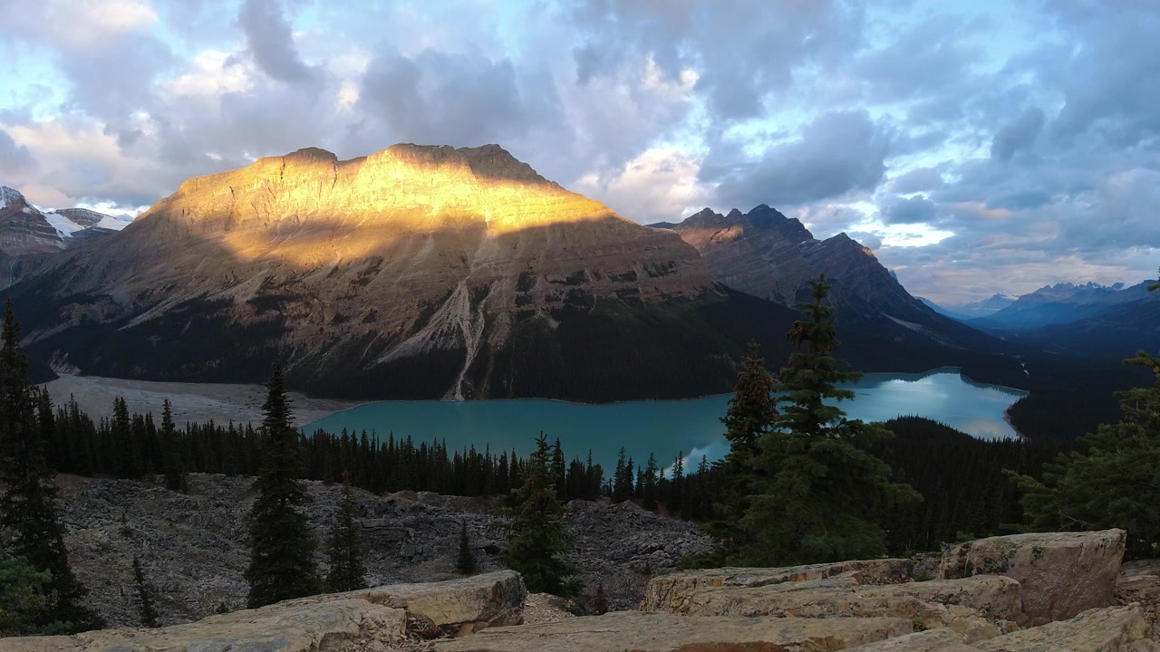 Le nuvole si illuminano mentre la luce dell'alba si diffonde lentamente sulle montagne sopra il lago turchese Peyto in questa ampia ripresa timelapse