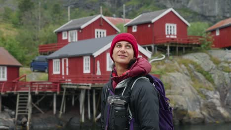 slow motion 360 orbit around a young female photographer tourist admiring the beautiful fisher village of å and its red rorbu houses in the lofoten islands, norway