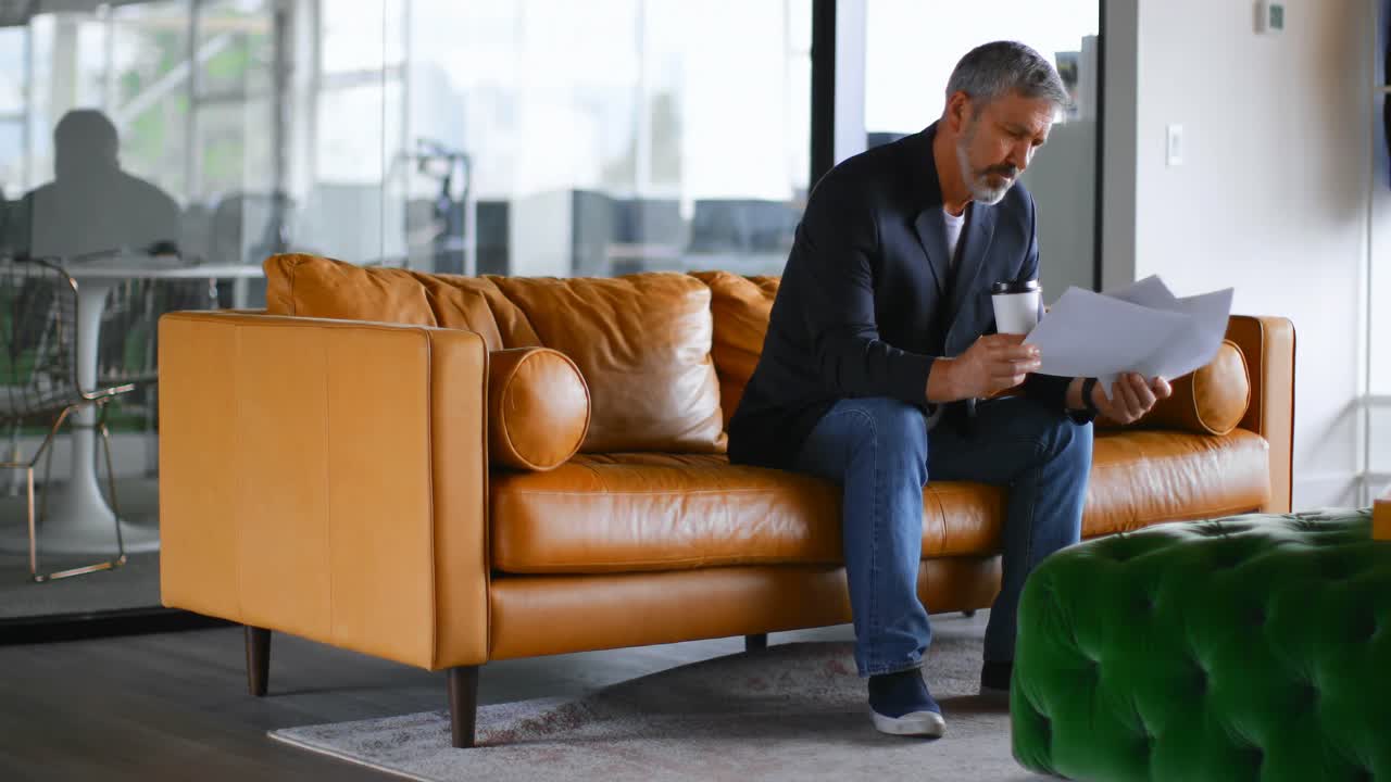 hombre de negocios con taza de café comprobando el documento en el sofá 4k
