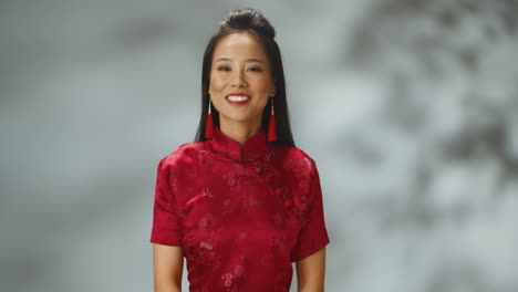 portrait shot of asian young cheerful woman in red traditional clothes smiling at camera