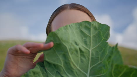 woman holding lettuce leaf in front of face closeup. smiling lady examining kale