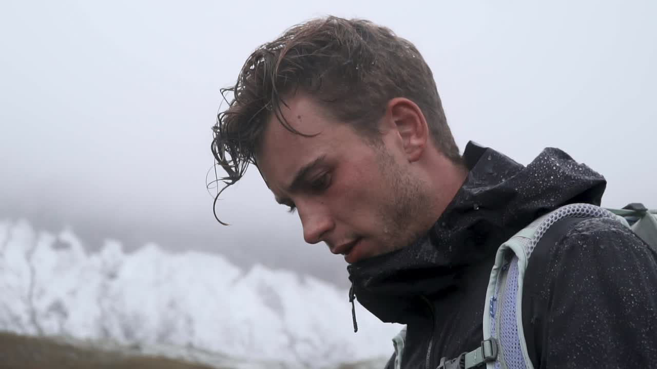 Slow motion close up shot of hiker in foggy and rainy mountain environment looking up into the distance