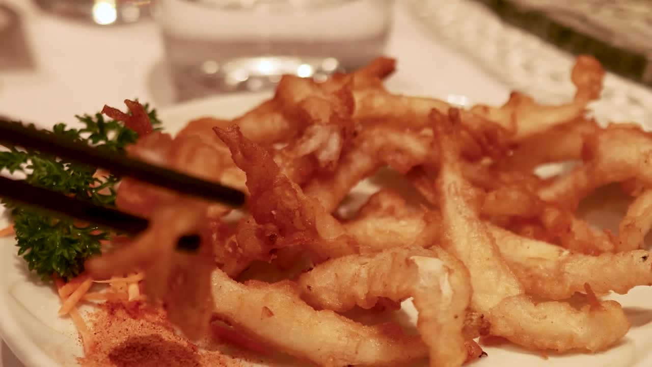 Um close-up de pauzinhos levantando peixe frito dourado de um prato decorado