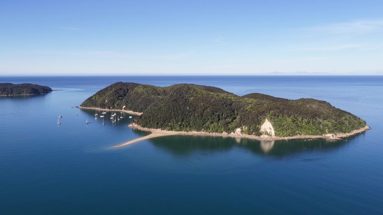 Vista aérea de una isla boscosa con veleros anclados en aguas costeras tranquilas.