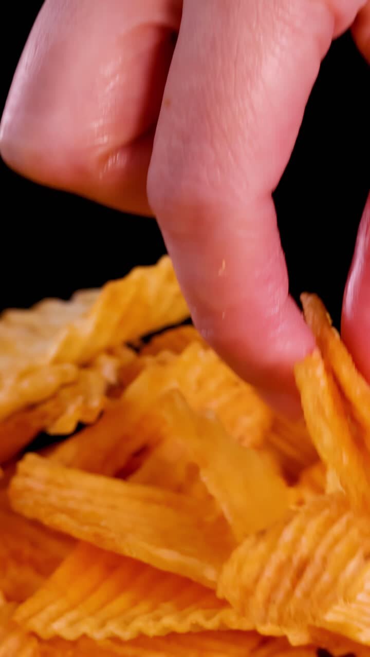 Human hand selects and lifts ridged potato chip from pile, studio lighting, close-up view