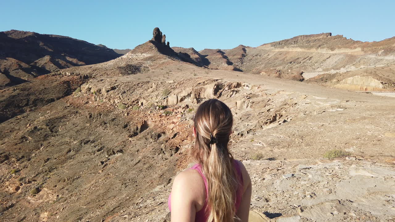 Jovem mulher observa as majestosas formações rochosas perto da Playa del Medio Almud, na ilha de Gran Canaria, município de Mogán.
