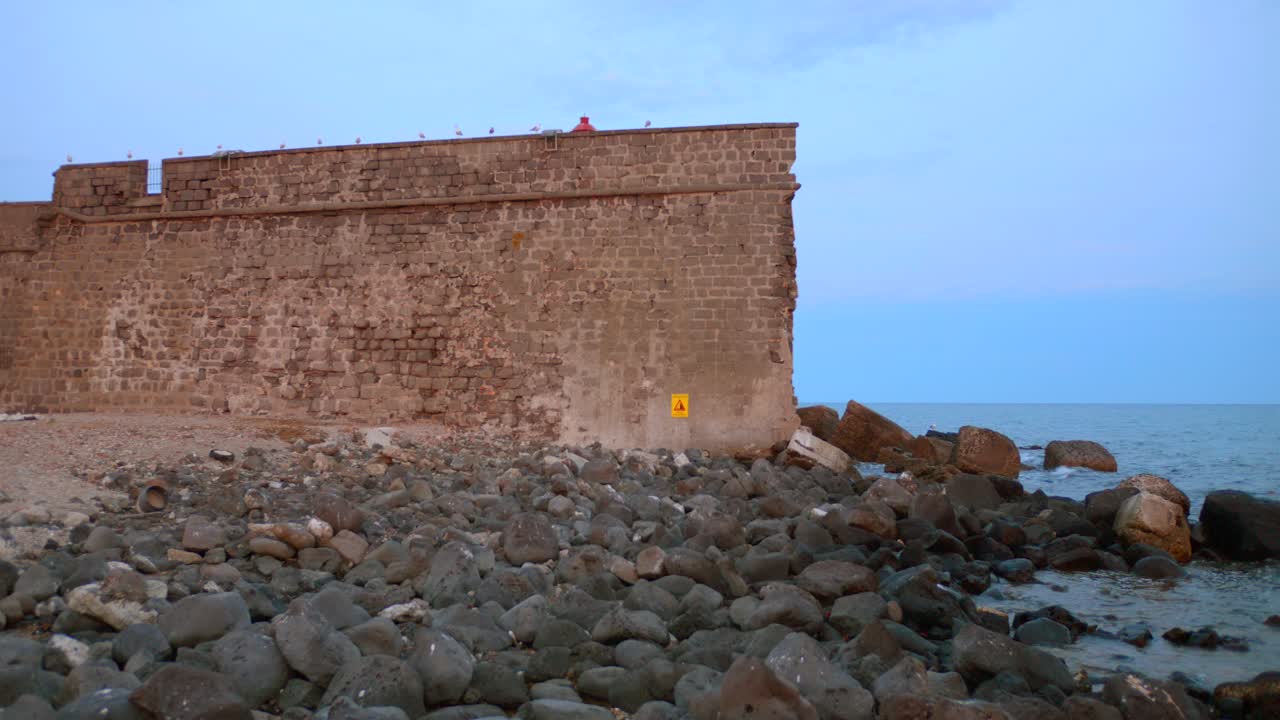 Stone fortress rises above dark volcanic rocks on Brescou Island, surrounded by sea and seabirds