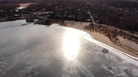 Aerial-view-over-a-chilly-beach-on-a-frozen-harbor-with-a-beautiful-coastline-at-sunset,-drone-shot,-travel-concept