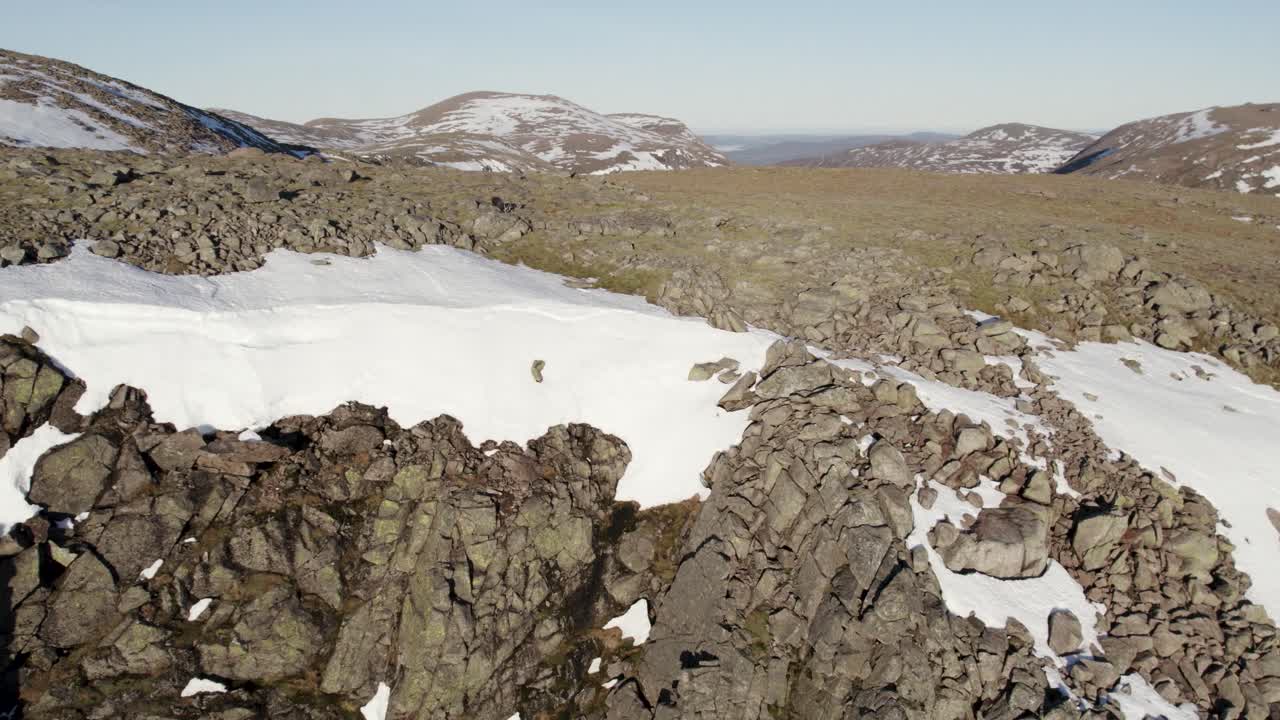 imágenes aéreas de drones que dan marcha atrás sobre un acantilado rocoso que revela un barranco empinado y dramático lleno de nieve con cielos azules claros en las montañas cerca de ben macdui en el parque nacional de cairngorms, escocia