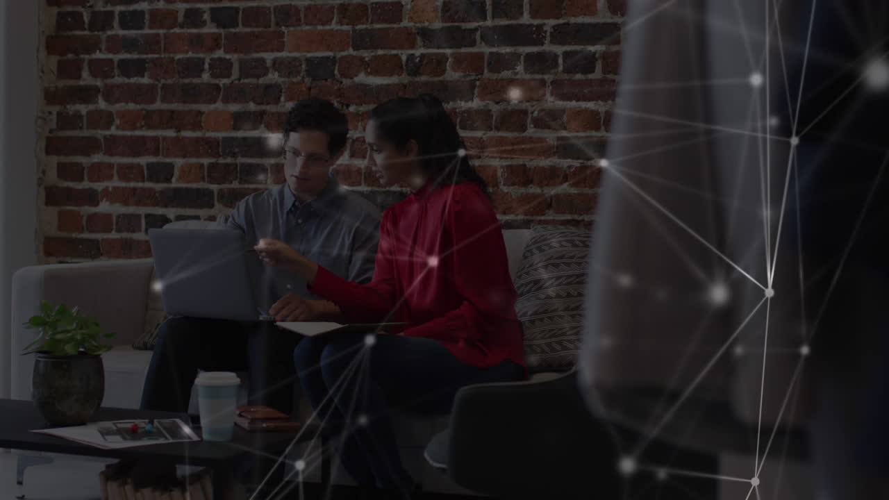 Animation of network of connections over male and female colleague using laptop on couch in office
