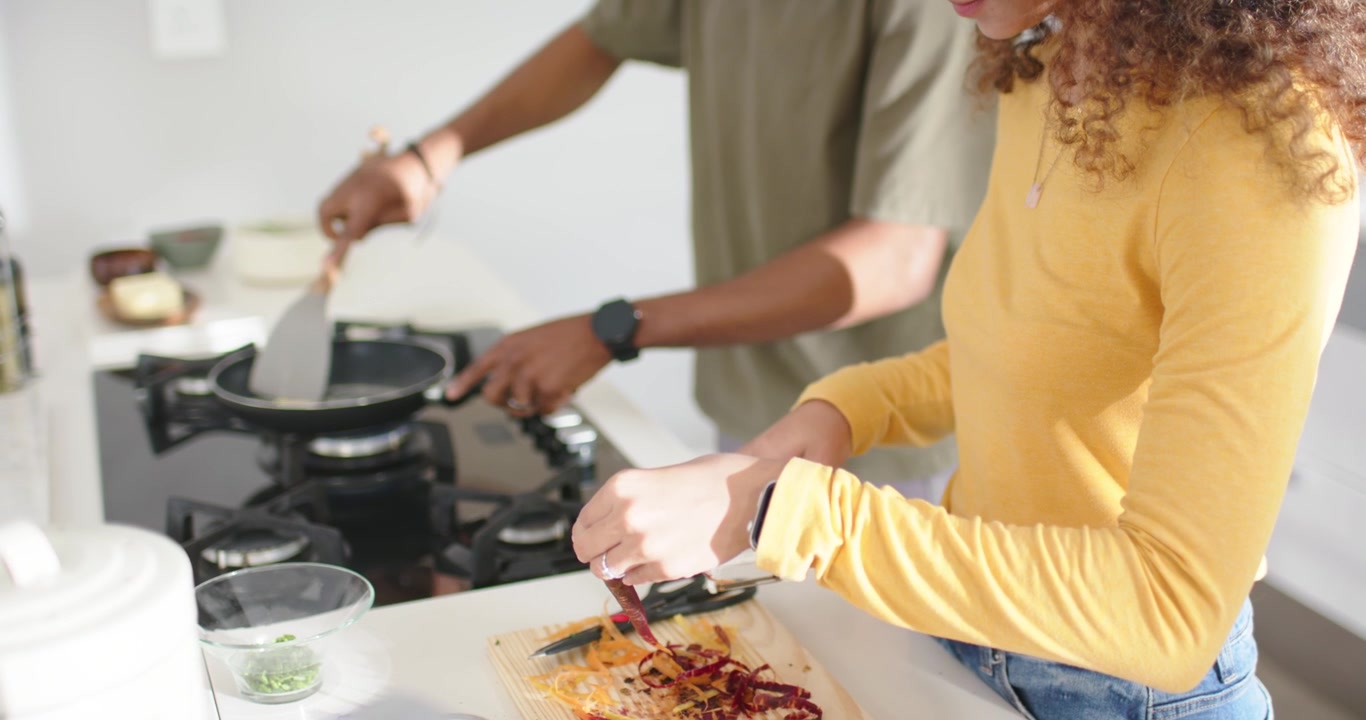 Coppia che cucina in cucina, l'uomo che mescola una padella con una spatola mentre la donna taglia le verdure per cena.