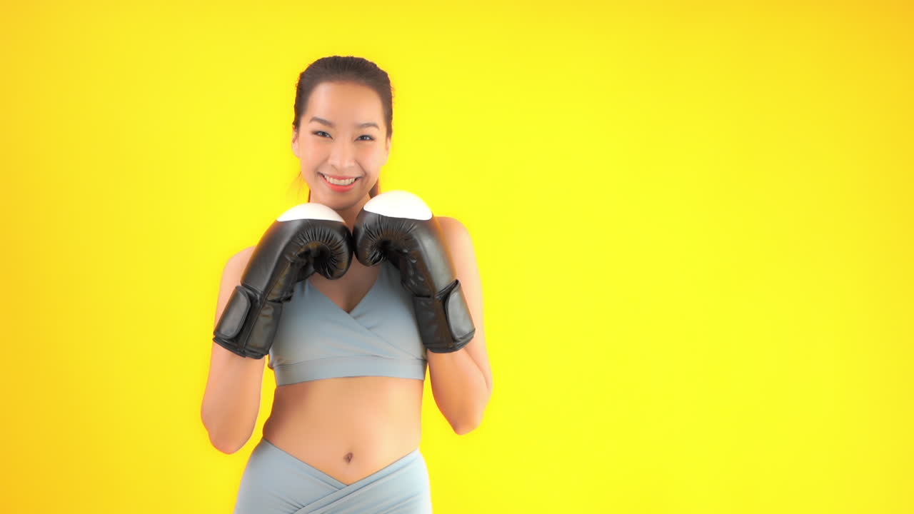 Pretty asian female with boxing gloves is ready for fight, full frame slow motion. Sport and fitness concept, isolated on yellow background