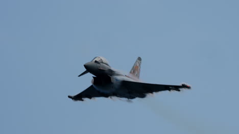 military jet aircraft flying fast and low with visible vapor trails around the wings against clear blue sky