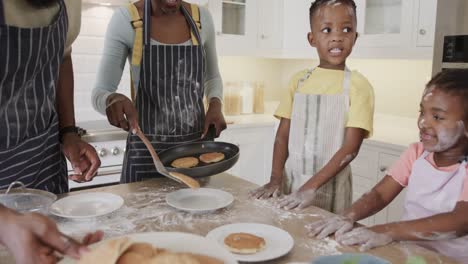 happy african american couple with son and daughter serving pancakes in kitchen, slow motion