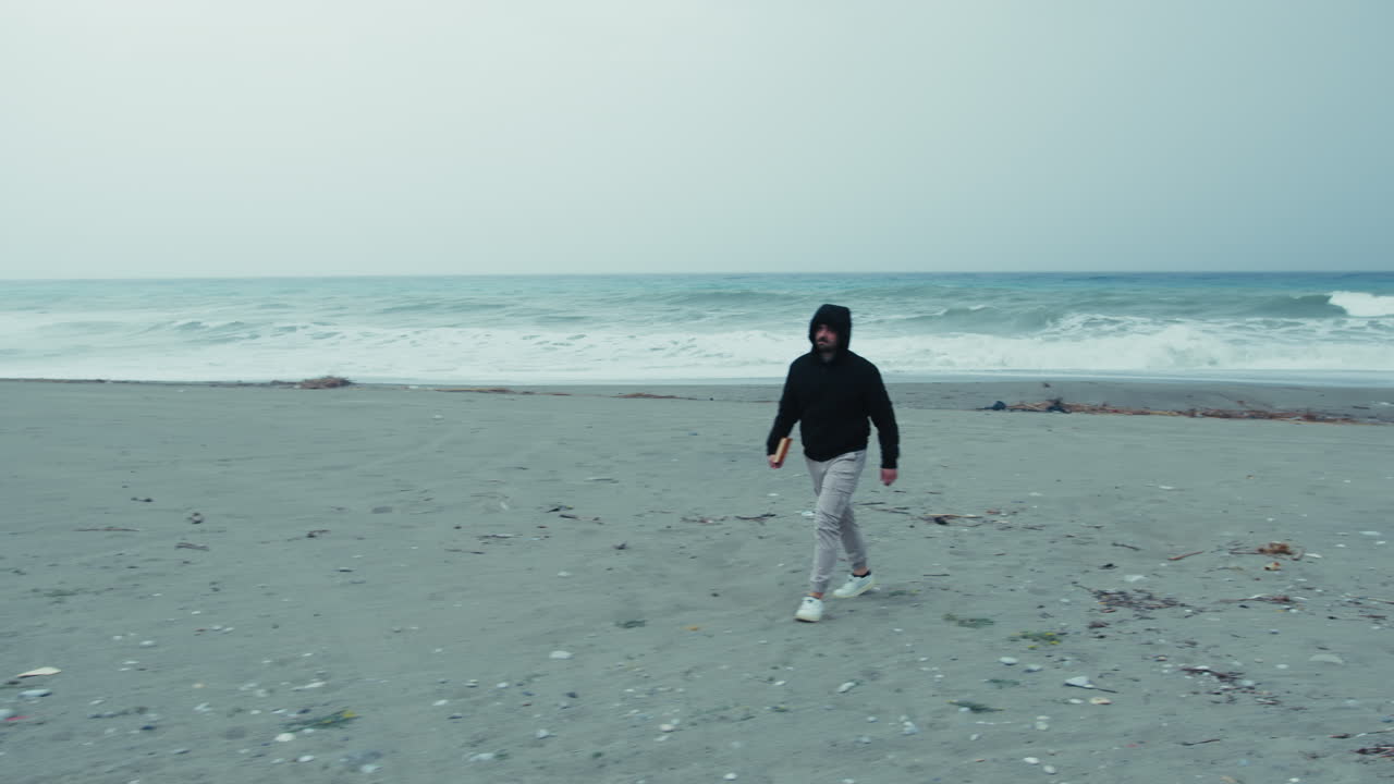 Man Holding A Book Walking Alone Near The Sea In Winter