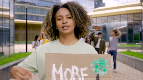 woman talking, walking and showing more trees less lies placard to the camera