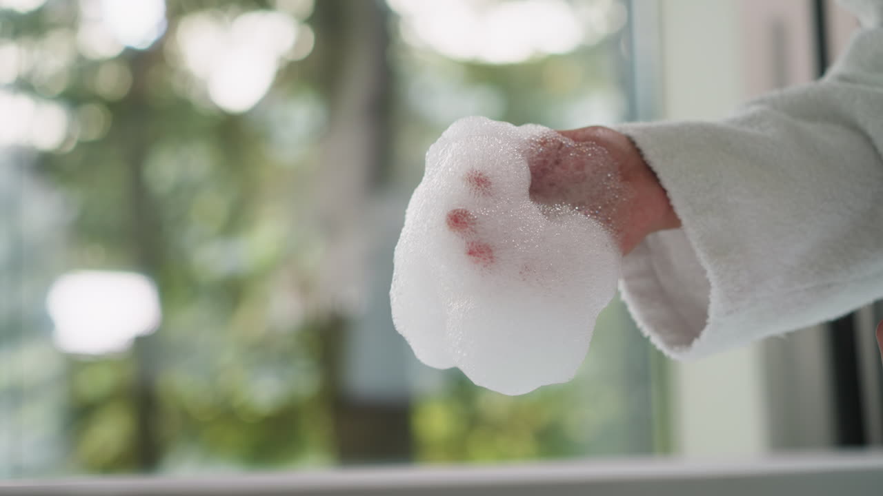 Woman gently touches soft bubble bath closeup. Lady in terry bathrobe holds foam cherishing calming aroma in morning. Body care procedures at home