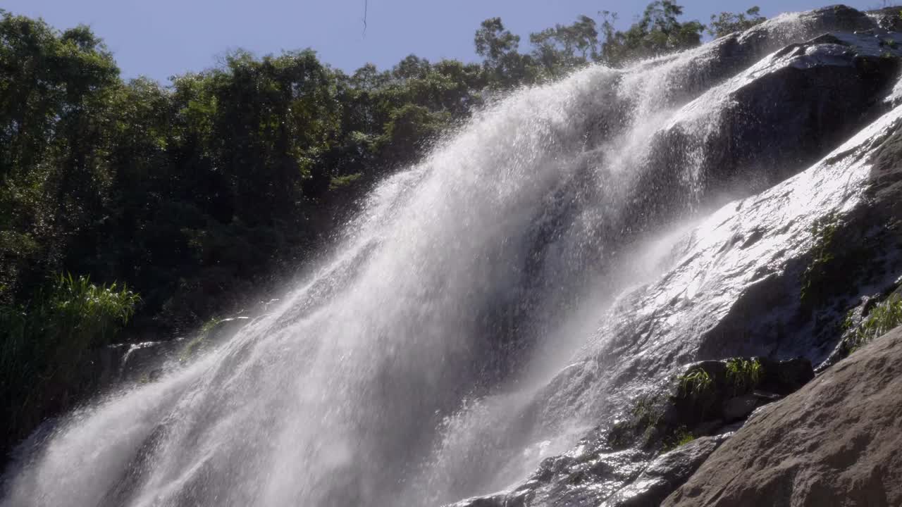 ángulo bajo mirando hacia los rápidos que fluyen rápidamente estrellándose sobre la cascada de rocas rocosas con árboles a la vista