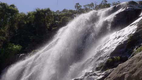 Low-angle-looking-up-at-fast-flowing-rapids-crashing-over-rocky-boulders-waterfall-with-trees-in-view-to-side