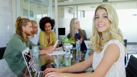 Mujer-Sonriente-Usando-Una-Computadora-Portátil-Mientras-Sus-Colegas-Interactúan-En-Segundo-Plano-4k