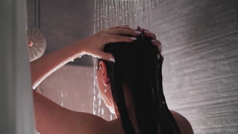 la mujer se lava la cabeza en la ducha moderna en casa. la dama morena acaricia la cabeza en una ducha grisácea con pared de azulejos. la rutina de limpieza trae placer a la dama