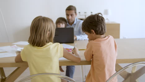 children playing and drawing at home under supervision of father