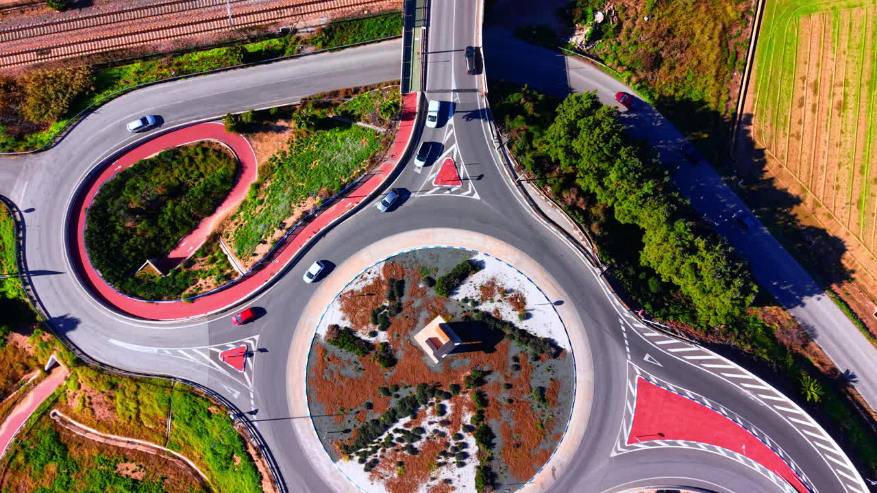 Road roundabout with red asphalt bike lanes and vehicles moving through the intersection. Top view of a circular traffic roundabout with cars