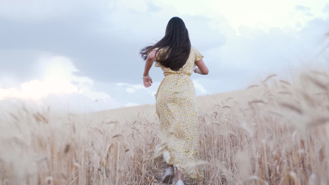 Back view of a carefree woman enjoying nature while running through a wheat field.