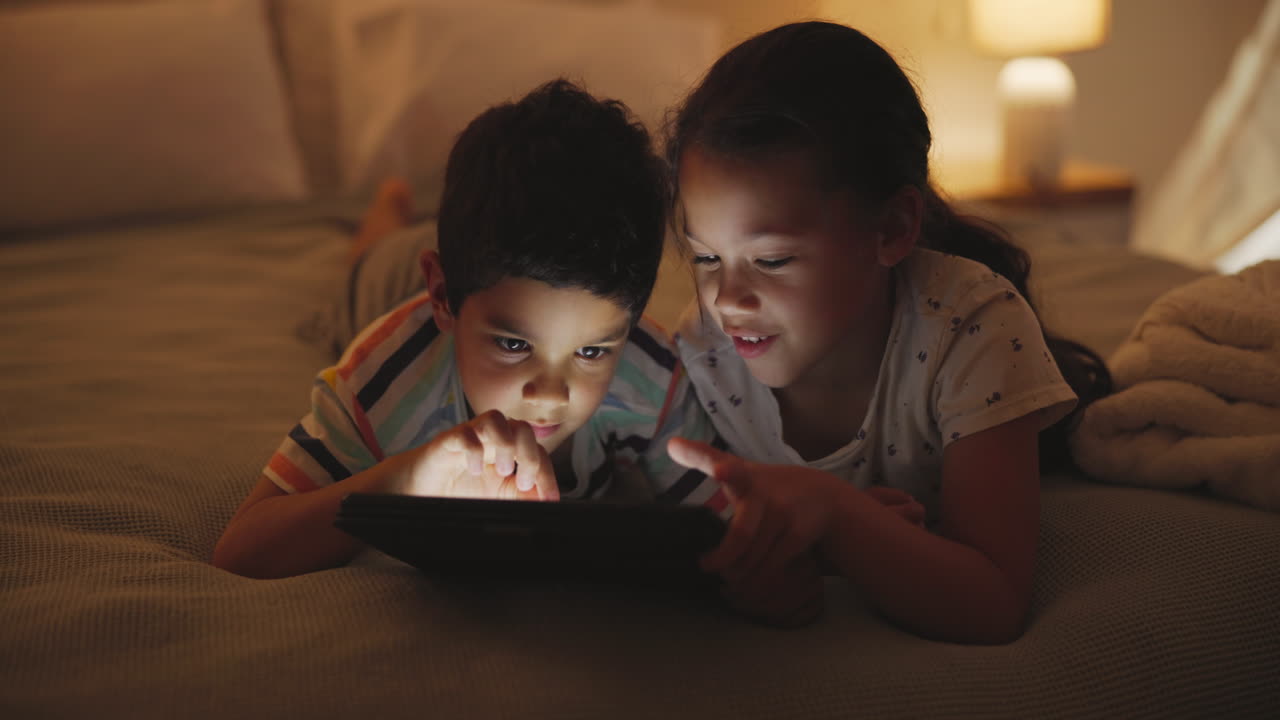 niños que usan una tableta en la cama por la noche