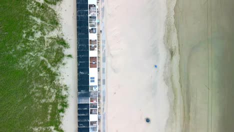 Vista-Panorámica-A-Vista-De-Pájaro,-Dunas-De-Arena,-Pequeñas-Cabañas-En-La-Playa-Y-Vistas-Al-Mar-Del-Norte