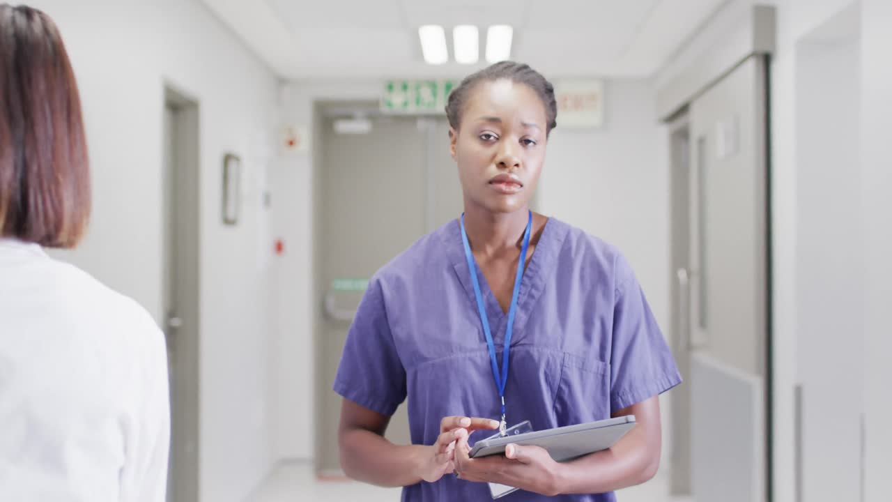 Video of african american female doctor walking in busy hospital corridor, using tablet, copy space