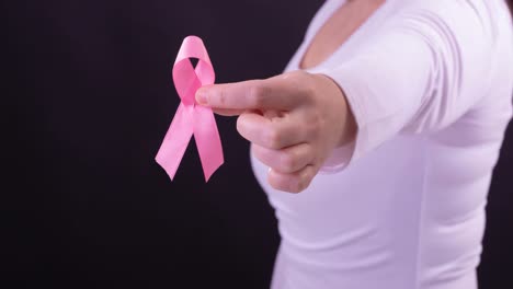 Video-of-midsection-of-caucasian-woman-holding-pink-cancer-awareness-ribbon,-with-black-background