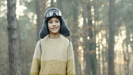 Little-Caucasian-boy-dreamer-of-being-a-pilot-in-hat-and-special-glasses-smiling-at-the-camera-in-the-forest