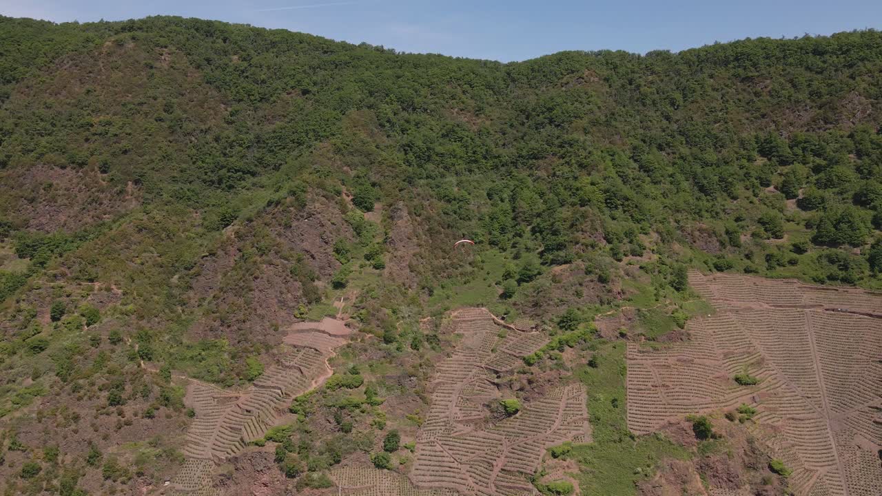toma panorámica aérea de la vasta cordillera con puntos de plantación en capas y un individuo que se lanza en paracaídas colina abajo