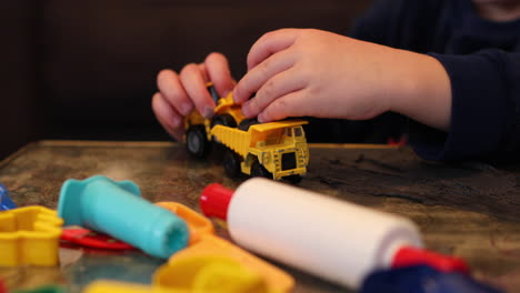 un primer plano de las manos de un niño jugando con su excavadora de remolque y arcilla adentro durante el encierro