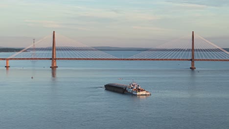 aerial view of cargo ship passing under cable-stayed bridge on parana river at sunset