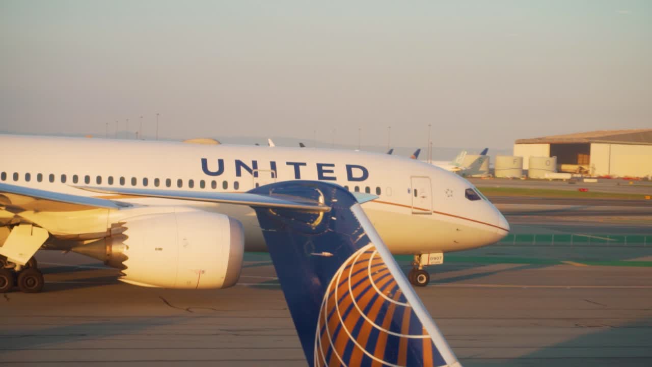 Profile panning mid shot of united airlines flight taxiing to runway on sunny sunset evening.